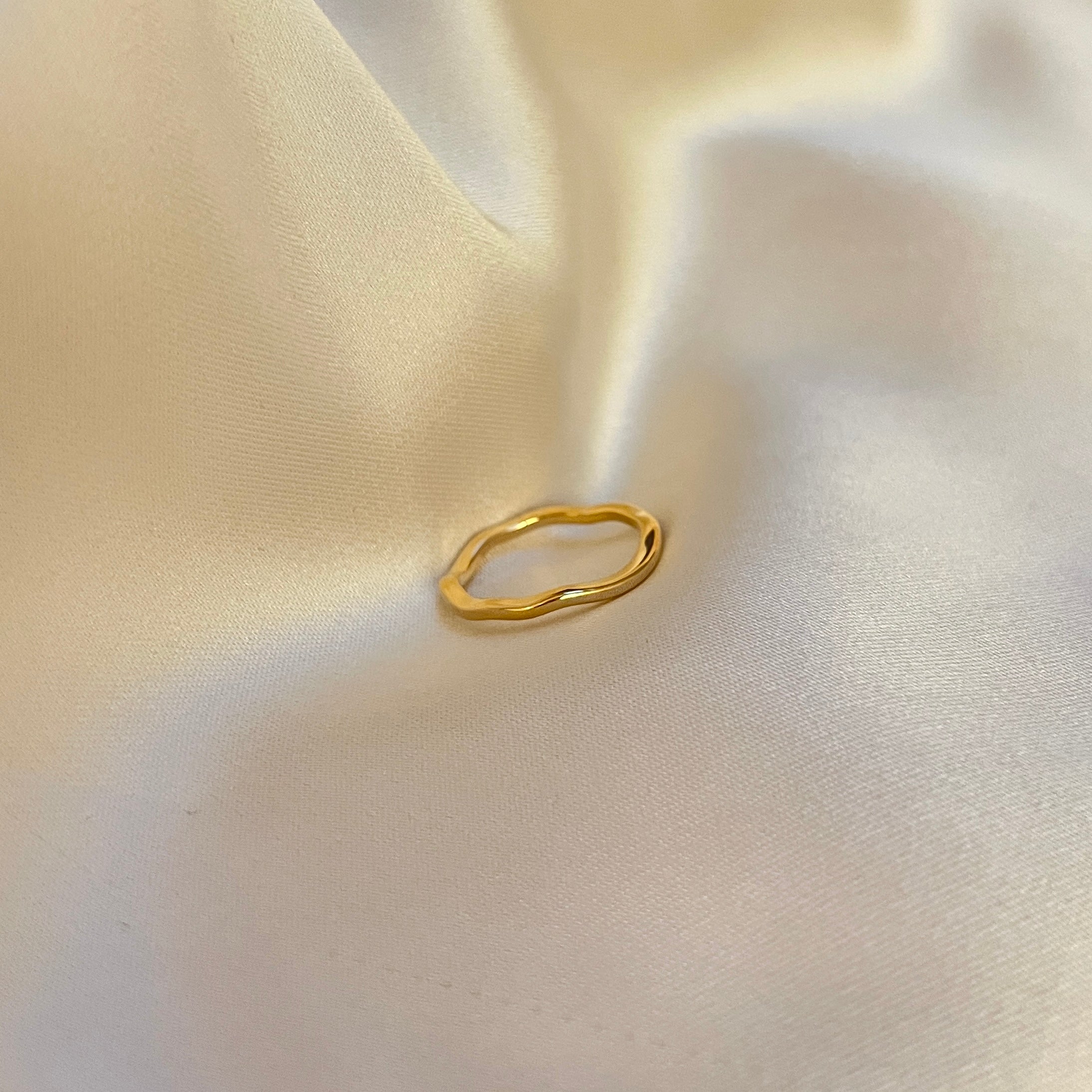 Faye Flow Ring – tunn guldfärgad ring med mjukt böljande, organisk form. Perfekt att bära ensam eller i stacking. Tillverkad i vattentåligt och allergivänligt rostfritt stål med PVD-plätering – ett stilrent smycke som håller säsong efter säsong.