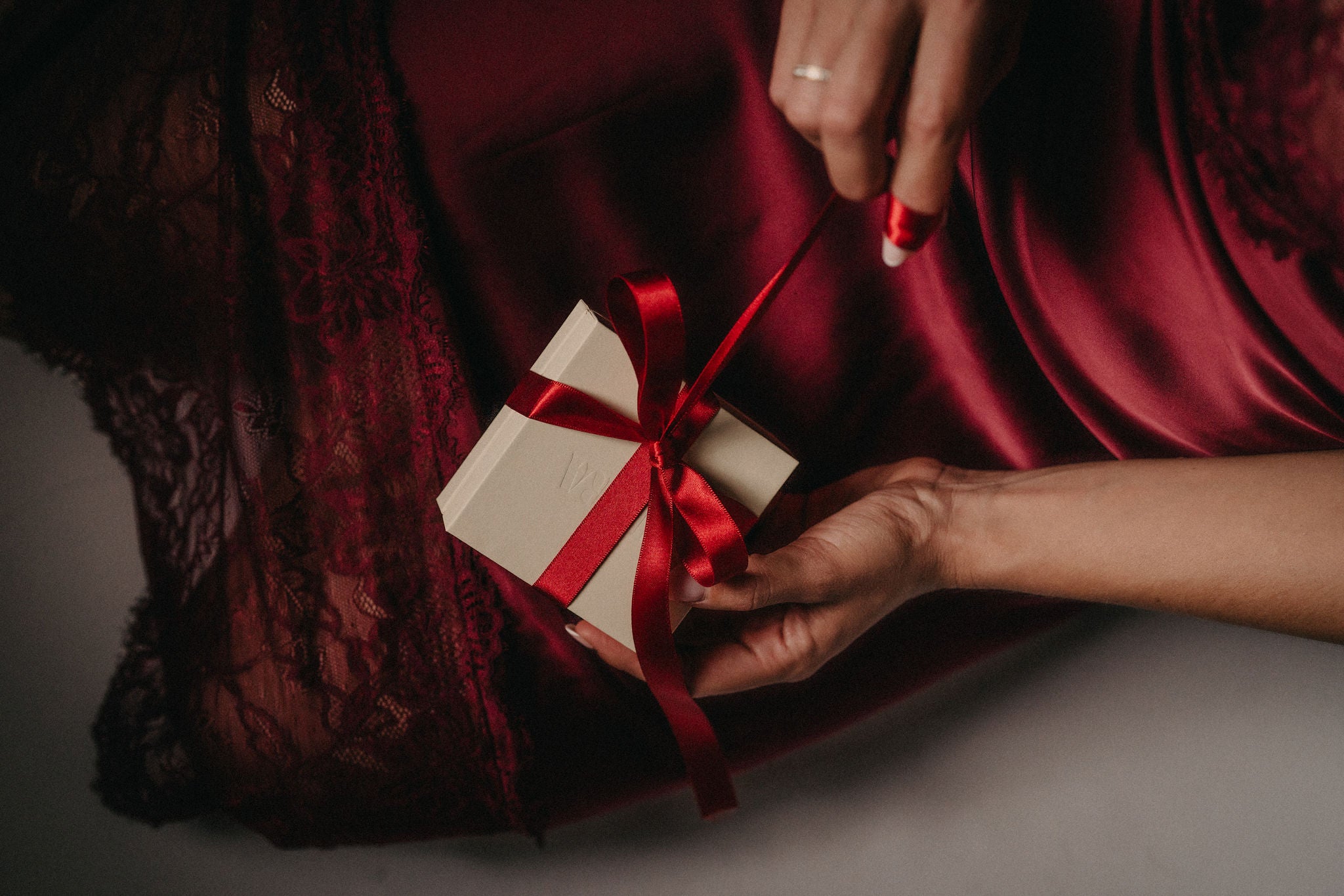 Hand som knyter rött sidenband runt Alora Avenue-presentask – elegant julinslagning av smycken i butter yellow-box. Perfekt julklapp till kvinnor, färdig att ge bort med hållbara, vattentåliga smycken som varar år efter år.