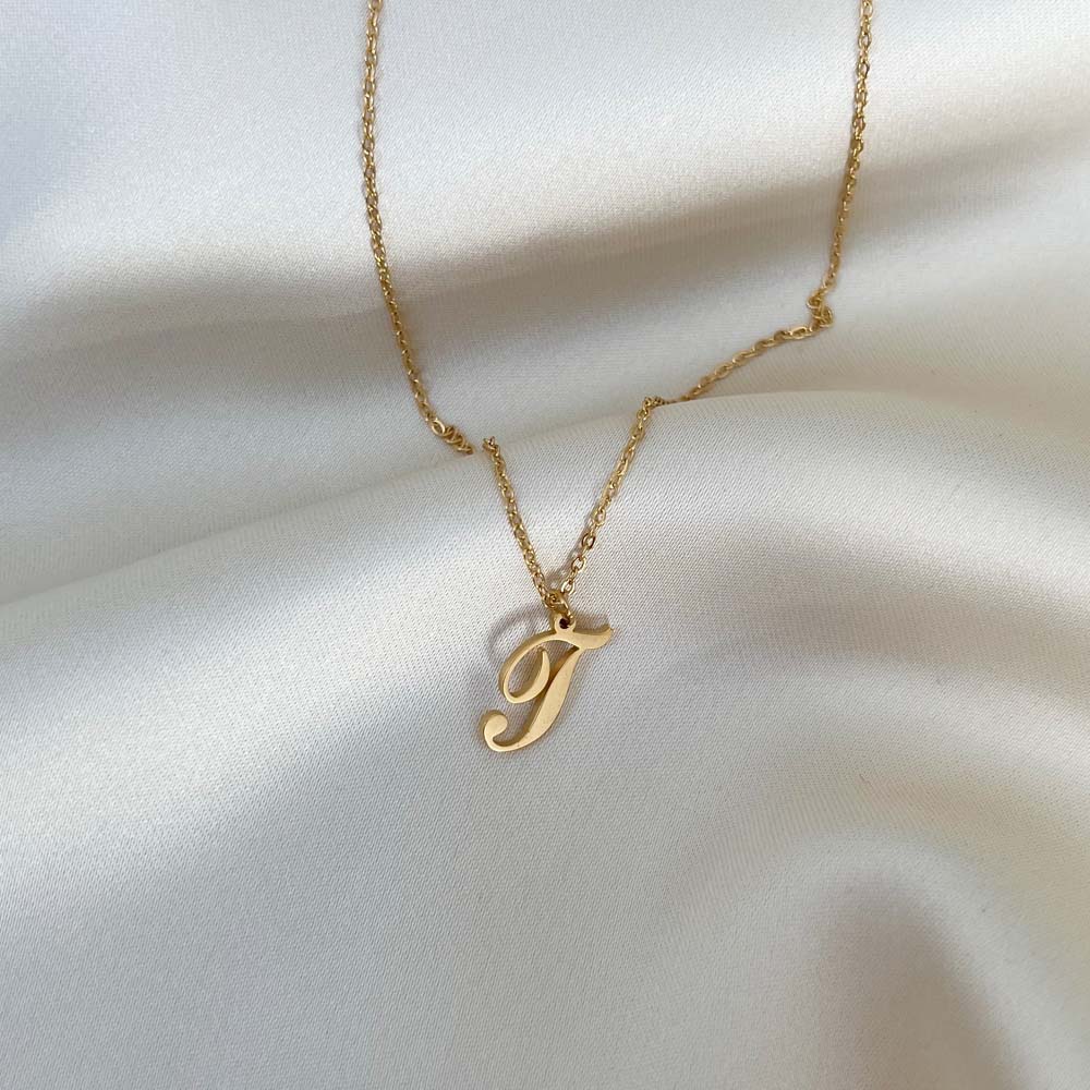 Alora Letter Necklace med bokstaven T i elegant skrivstil, ett tidlöst smycke tillverkat i PVD-pläterat rostfritt stål.