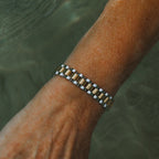 Analog Ava Wristband från Alora Avenue i närbild mot vattnets yta – ett vattentåligt och allergivänligt armband i silver och guldtoner med vintageinspirerad känsla. En tidlös accessoar med lyxig edge för henne som vågar sticka ut med detaljer som räknas.