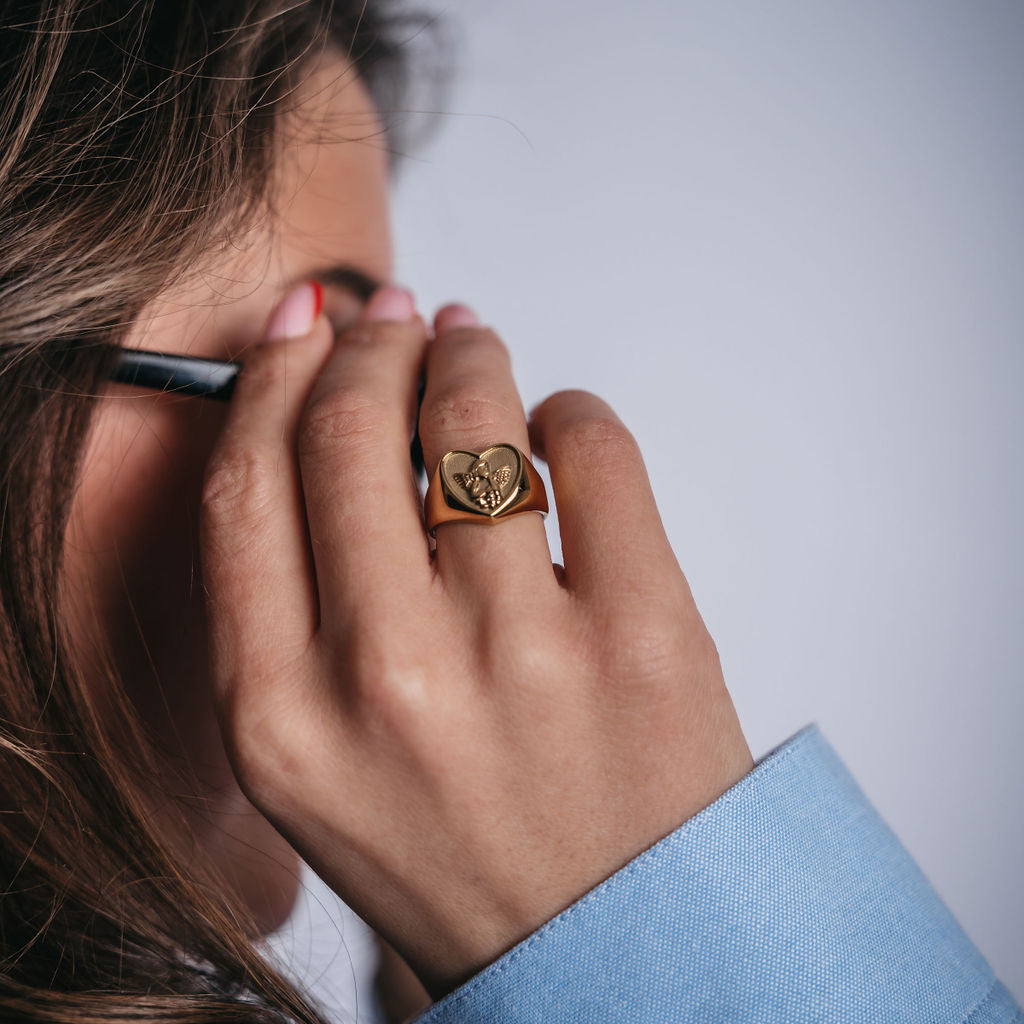 Angelic Love Ring i guld – en hjärtformad statementring med vackert ingraverat ängelmotiv. En vattentålig och allergivänlig favorit från Alora Avenue, skapad för dig som bär ditt hjärta med stolthet.