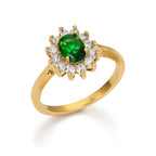 Celine Carmosé Ring är en elegant guldring med en grön sten i centrum, omgiven av gnistrande vita stenar, tillverkad i rostfritt stål med PVD-plätering.