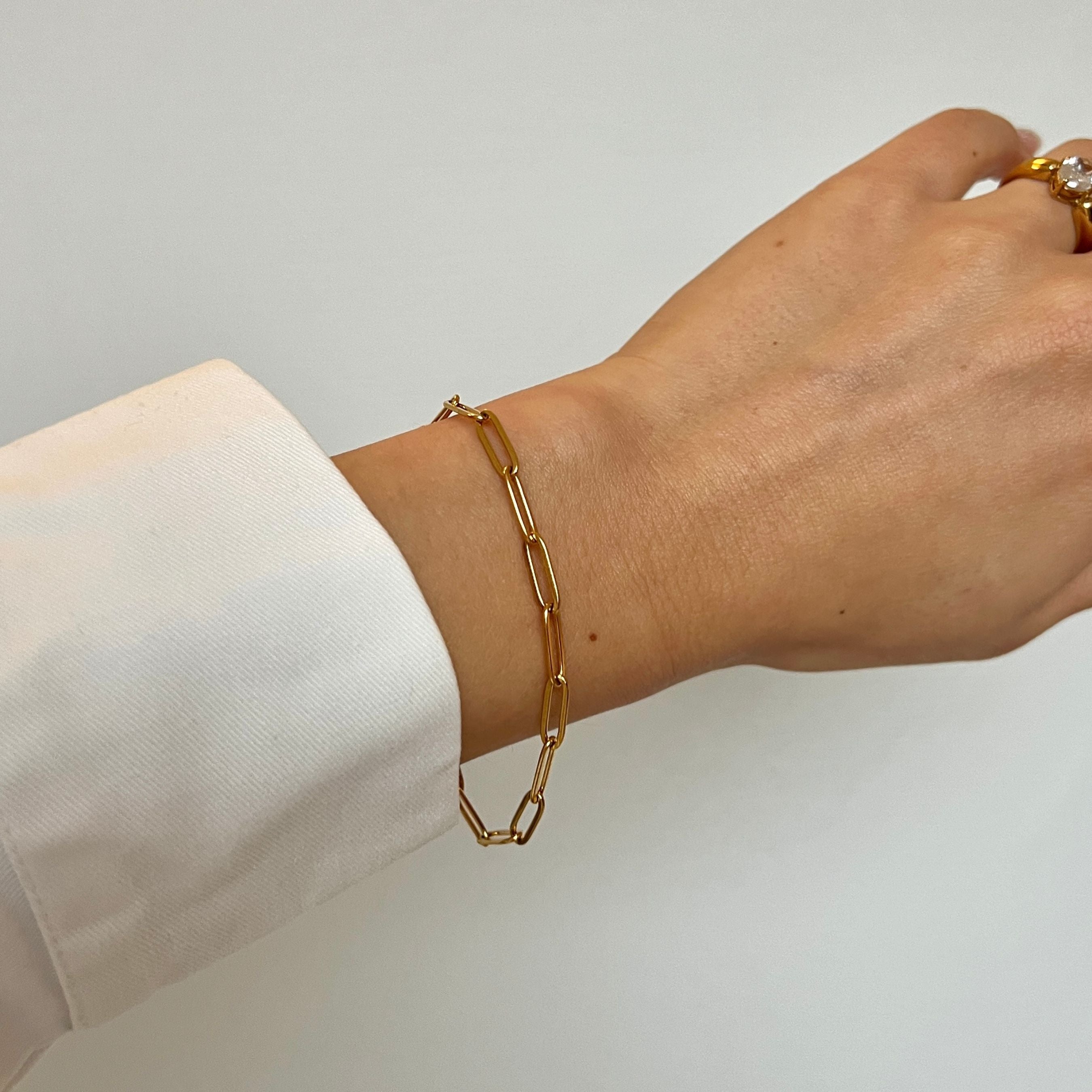 Dawn Clip Bracelet på en kvinnas arm, perfekt guldfärgat paperclip-armband i rostfritt stål med slitstark PVD-plätering, vattentåligt och hållbart.