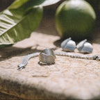 Närbild på Hedwig Huggie Ring från Alora Avenue i silver, fotograferad i varmt solljus på kalkstensyta bredvid gröna citrusfrukter. En vattentålig och allergivänlig ring i rostfritt stål med skulptural form – perfekt för dig som vill bära stil med karaktär varje dag.