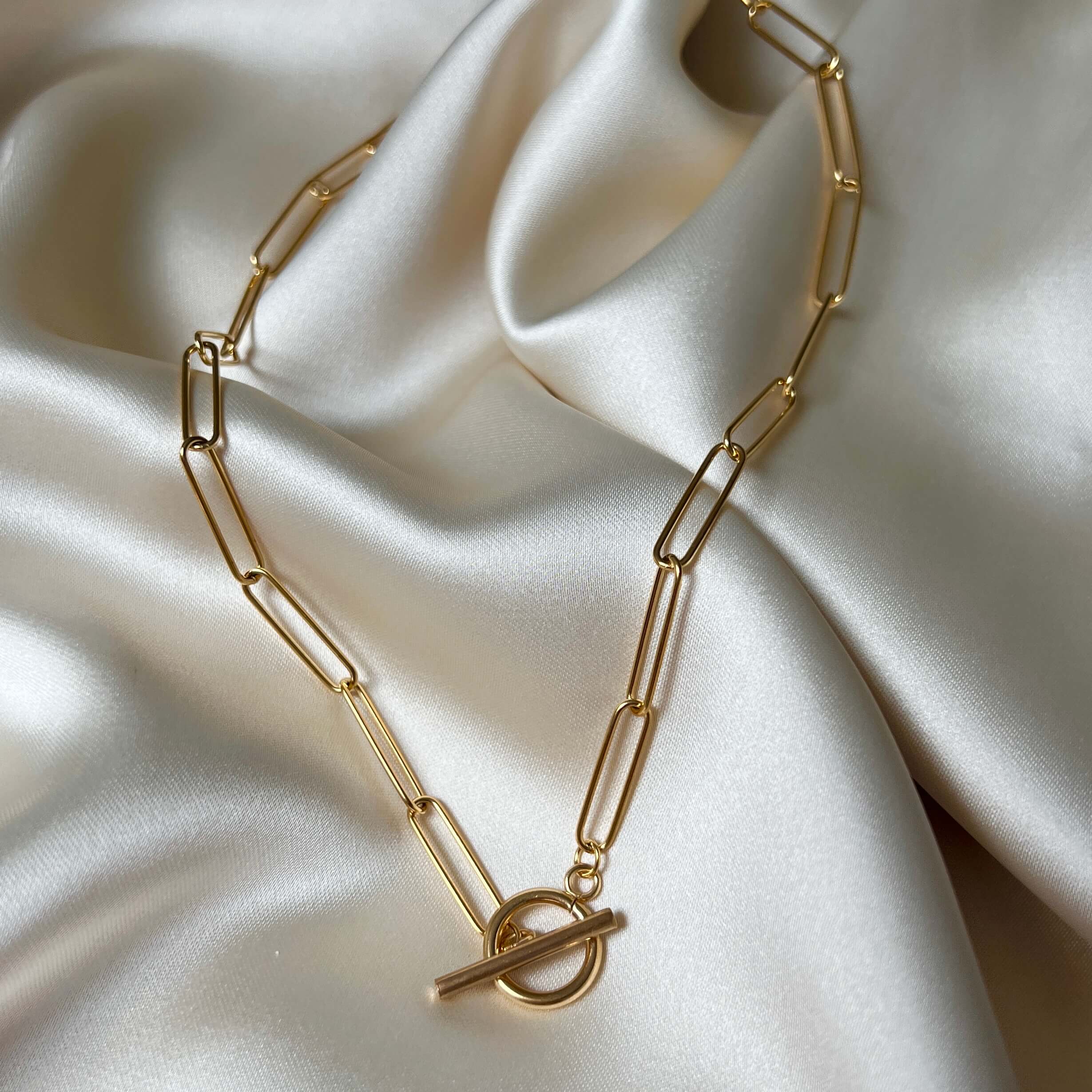 Lana Lotus Necklace – guldfärgad paperclip-kedja med unikt T-lås, elegant design och slitstark PVD-plätering för långvarig glans.