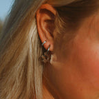 Närbild på Lily Dream Loops örhängen i silverfärgat rostfritt stål, formade som blommor. Vattentåliga och allergivänliga örhängen från Alora Avenue – stilrena, tidlösa och perfekta att bära varje dag.