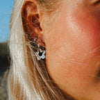 Närbild på Lily Dream Loops örhängen i rostfritt stål, formade som blommor. Vattentåliga och allergivänliga örhängen från Alora Avenue, perfekta för vardag och fest.