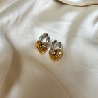 Lydia Love Loops från Alora Avenue – vattentåliga och allergivänliga örhängen i tvåtonad design med silvriga hoops och guldfärgade hjärtan. Fotograferade på glänsande satin – perfekta som kärleksfull gåva eller statement-accessoar med edge och elegans.