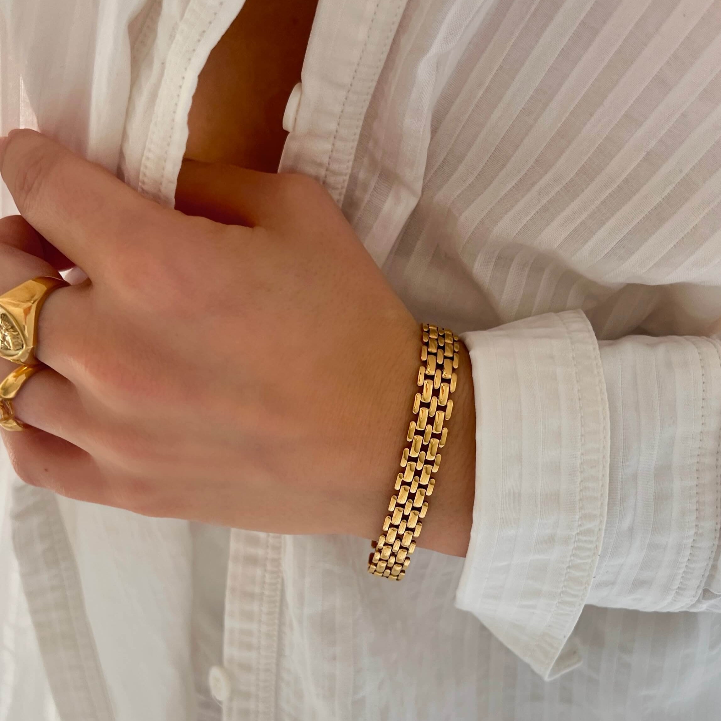 Maya Magnolia Bracelet – exklusivt guldarmband med bred länkdesign i blank finish, bärs till vit skjorta för en sofistikerad look från Alora Avenue