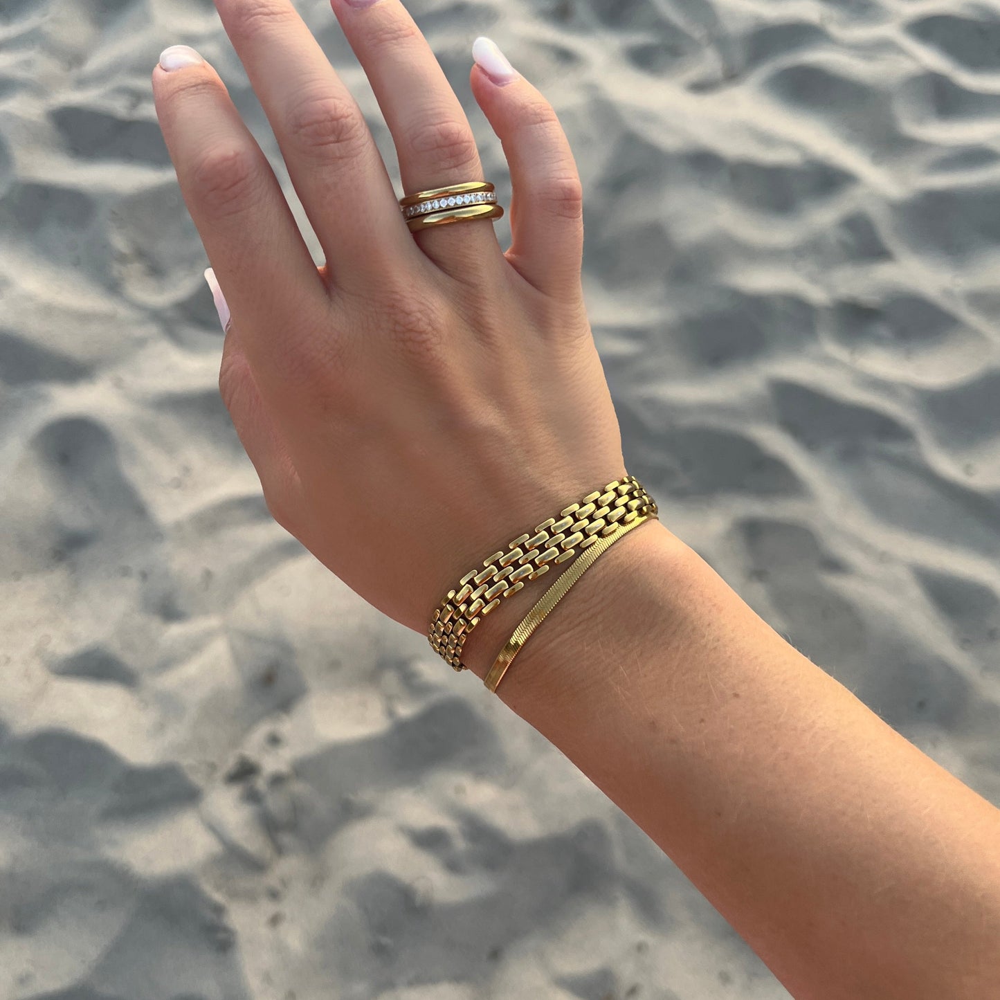 Stilfull Maya Magnolia Bracelet på kvinnas arm vid stranden, med guldigt armband och vattentålig PVD-plätering som glänser i solens ljus.