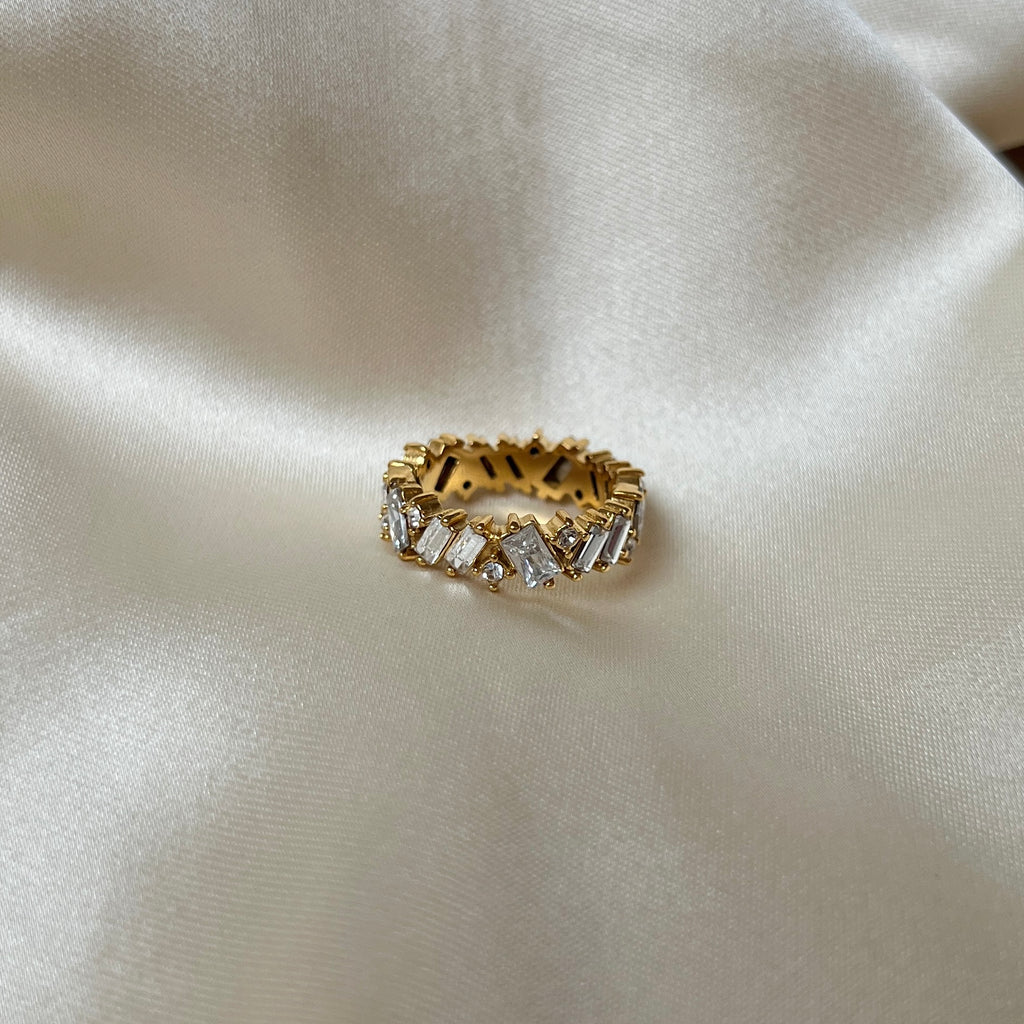Messy Crystal Ring från Alora Avenue fotograferad på champagnefärgat tyg – guldfärgad ring med lyxig känsla, prydd med oregelbundet slipade kristaller. Perfekt för dig som vill ha ett vattentåligt, allergivänligt och glamoröst smycke som håller för vardag, strand och fest.