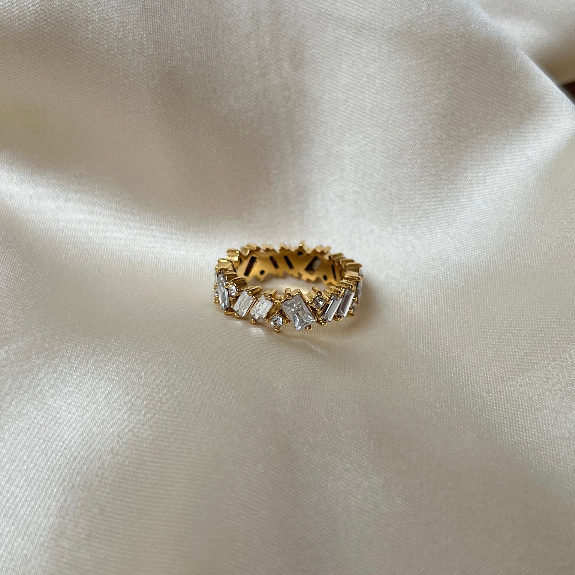 Messy Crystal Ring från Alora Avenue fotograferad på champagnefärgat tyg – guldfärgad ring med lyxig känsla, prydd med oregelbundet slipade kristaller. Perfekt för dig som vill ha ett vattentåligt, allergivänligt och glamoröst smycke som håller för vardag, strand och fest.