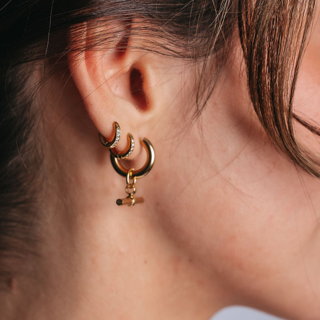 Mini Crystal Hoops från Alora Avenue – små, glittrande örhängen i guld med infattade kristaller, fotograferade i första hålet på örat tillsammans med större hoops. Vattentåliga och allergivänliga örhängen, perfekta för dig med flera hål i öronen eller som söker en stilren detalj med gnistrande finish.