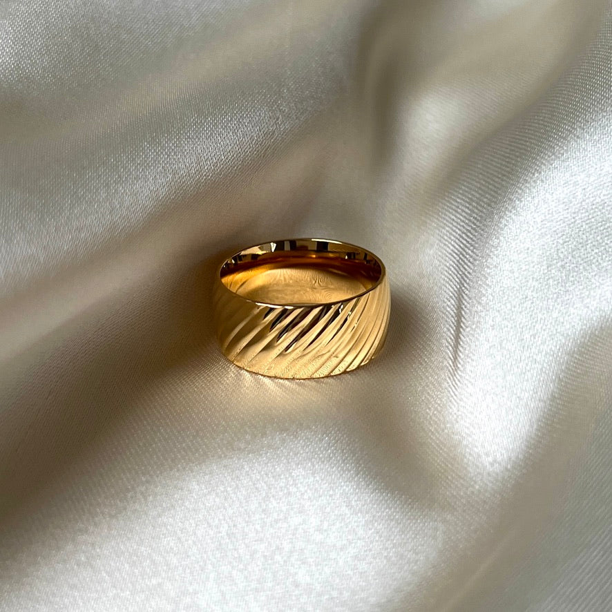 Oblique Orion Ring i guld med breda diagonala ränder, 9 mm bred. Tillverkad i allergivänligt rostfritt stål och PVD-pläterad i 18K guld, vattentålig och hållbar för dagligt bruk.