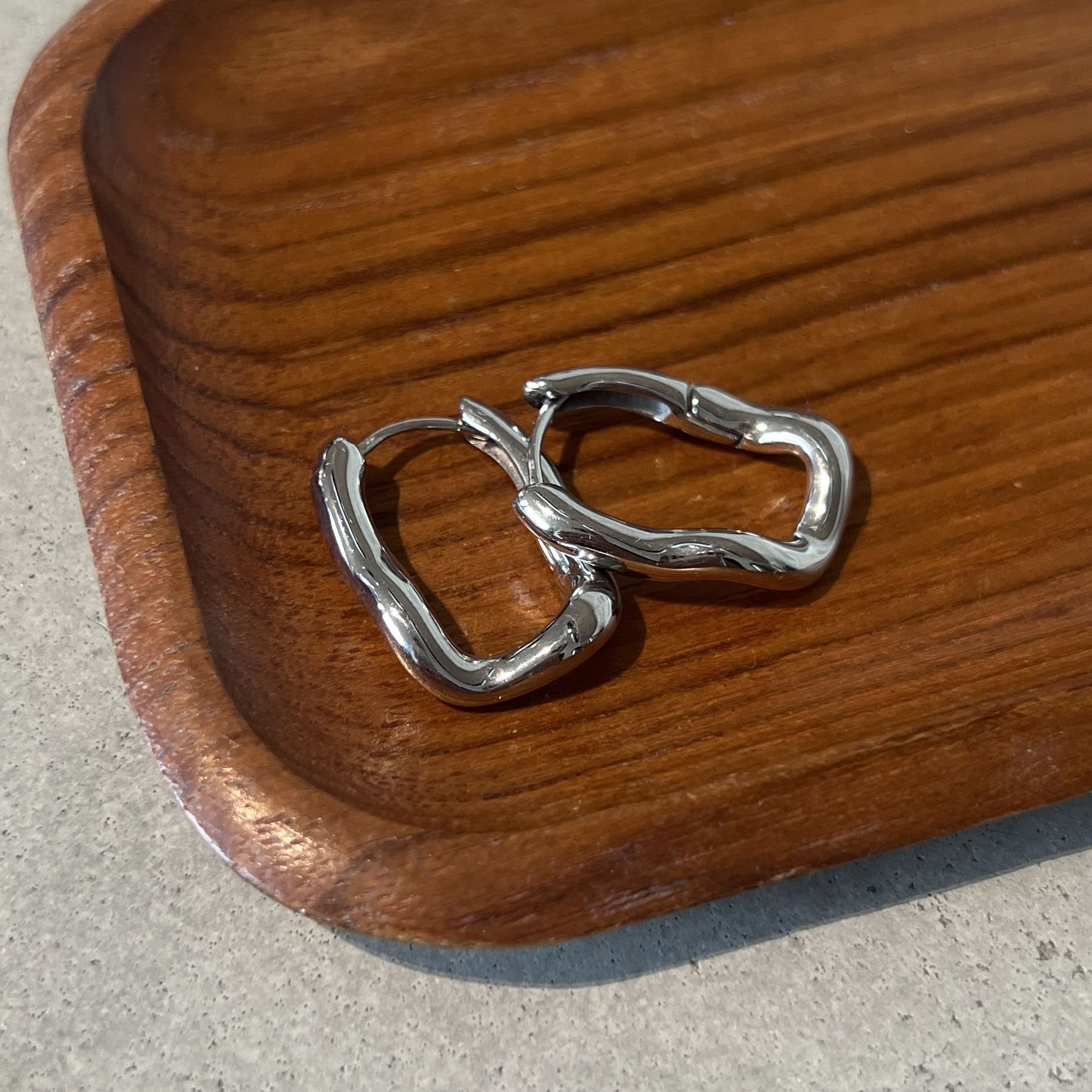Saint Penny Hoops i silver med asymmetrisk oval design, vattentåliga och tillverkade i rostfritt stål för långvarig hållbarhet.