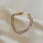 Santiago Sunstone Bracelet liggandes på ett glansigt, ljust tyg. Ett elegant tennisarmband med baguetteslipade kristaller infattade i guldtonad bas.