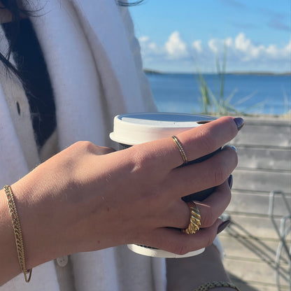 Shim Shim Ring på en kvinnas finger medan hon njuter av en kopp kaffe vid havet på västkusten. Den eleganta guldringen med cubic zirconia-stenar ger en subtil, gnistrande detalj i det natursköna landskapet