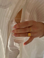 Shim Shim Ring från Alora Avenue på handen – en tunn guldfärgad ring med små gnistrande kristaller, fotograferad i mjukt morgonljus med ett glas i handen. Perfekt för en diskret men glittrande touch, vattentålig och allergivänlig.