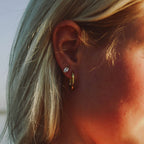 Stellar Serenity Hoops från Alora Avenue på modell, guldfärgade släta ovala creoler i rostfritt stål. Vattentåliga och allergivänliga örhängen med tidlös och elegant design – perfekta både till vardag och fest.