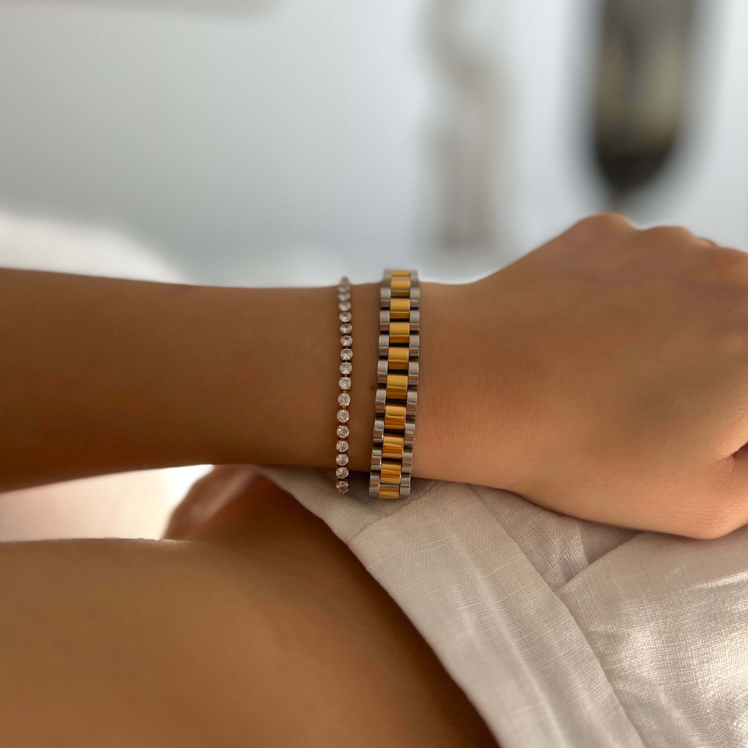 Tilda Tennis Bracelet från Alora Avenue – ett vattentåligt och allergivänligt tennisarmband i guldpläterat rostfritt stål med vita gnistrande stenar. Här stylat tillsammans med Analog Ava Armband i silver och guld – en tidlös kombination för både vardag och fest.