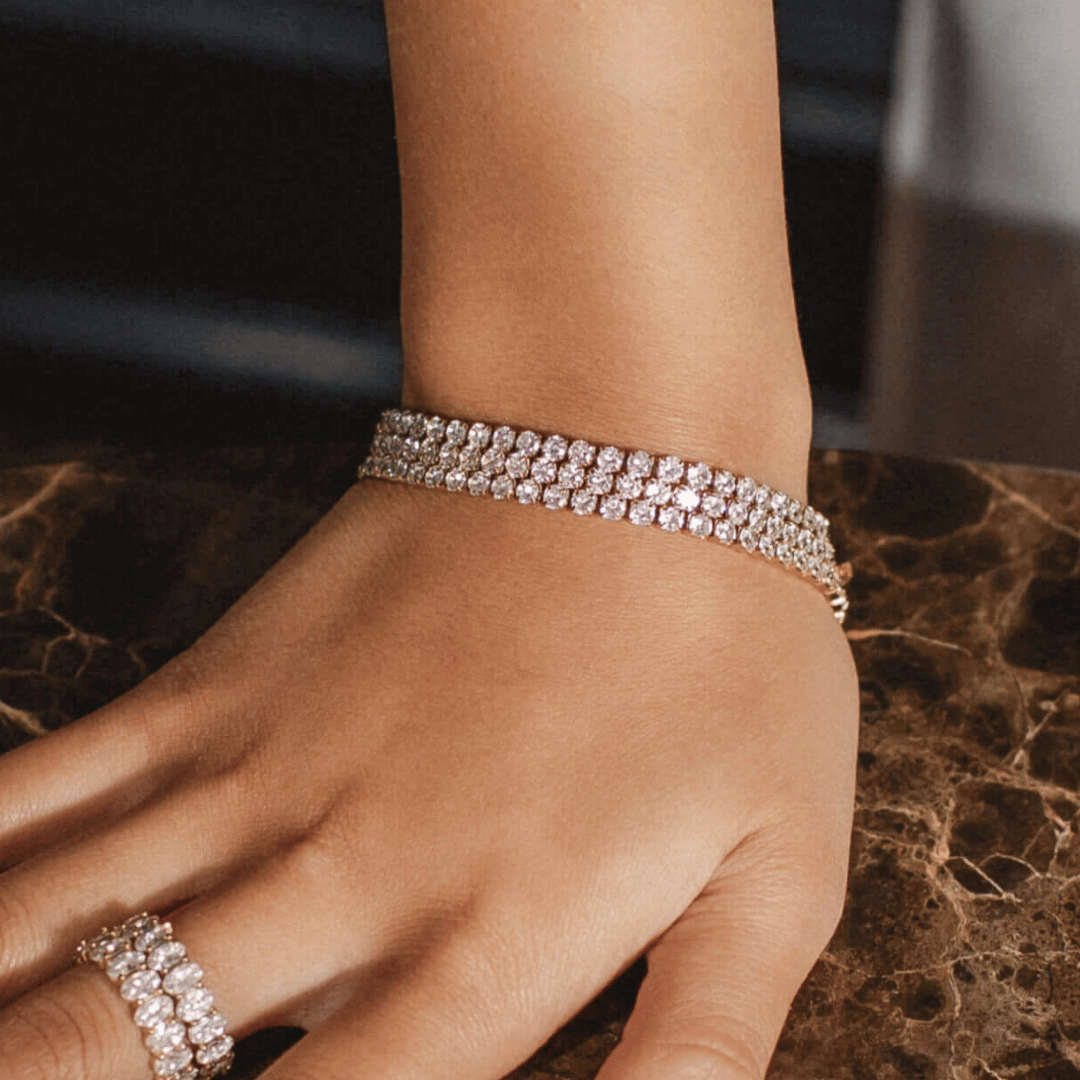 Tilda Tennis Bracelet, ett elegant guldigt tennisarmband med glittrande cubic zirconia-stenar, visar sin vackra design inklusive säker låsning och bekväm passform. Tillverkat i allergivänligt rostfritt stål och behandlat med hållbar PVD-plätering i 18K guld, glittrar det vackert mot en stilren bakgrund. Vattentåligt och perfekt för både vardag och fest.