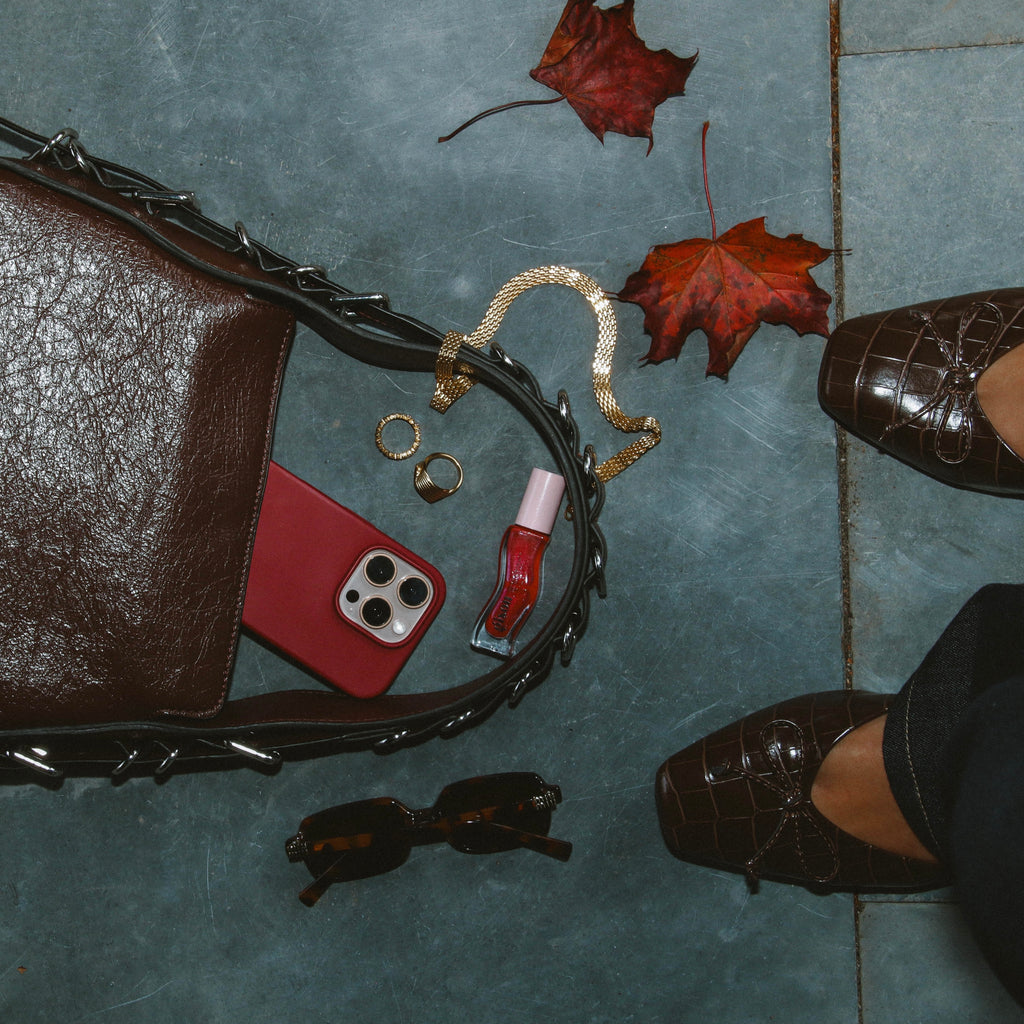 Airy Aurora Necklace i guld placerat i en elegant flatlay med höstlöv, väska och accessoarer. Stilrent och vattentåligt halsband från Alora Avenue – perfekt för vardagslyx.