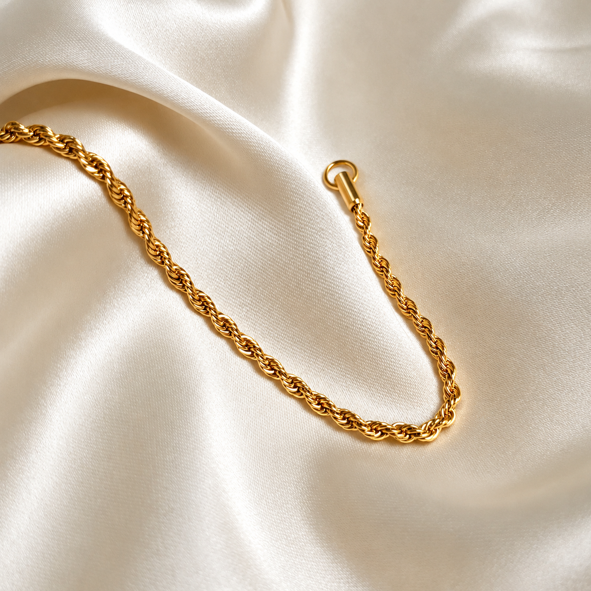 Aloe Allie Bracelet i guld fotograferad på ljust silkestyg. Vattentåligt och allergivänligt smycke i rostfritt stål med 18K PVD-guldplätering från Alora Avenue.