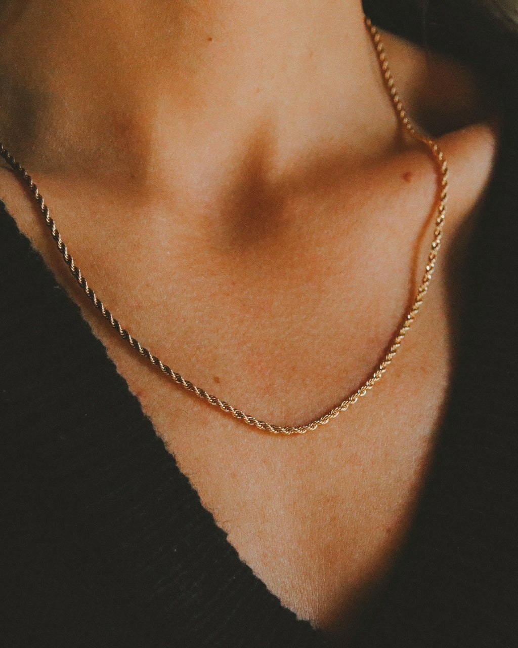 Close-up på modell som bär Aloe Aspen Necklace – en guldig snurrad cordellkedja i rostfritt stål med 18K guld PVD, vattentålig design och tidlös elegans.