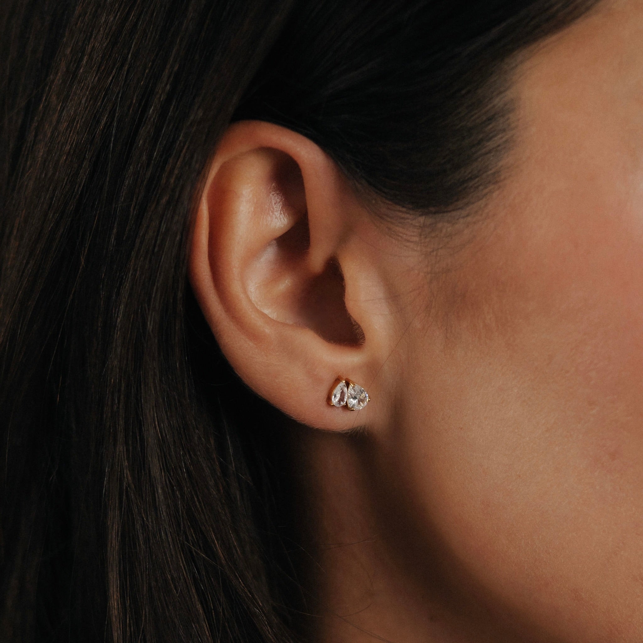 Dea Drop Earrings – dubbeldrop studs i 18K PVD-guld från Alora Avenue, med två glittrande stenar i droppform som reflekterar ljuset vackert. Designade för att tåla dusch, hav och vardag utan att tappa glans – en elegant lösning för den som vill bära smycken varje dag.
