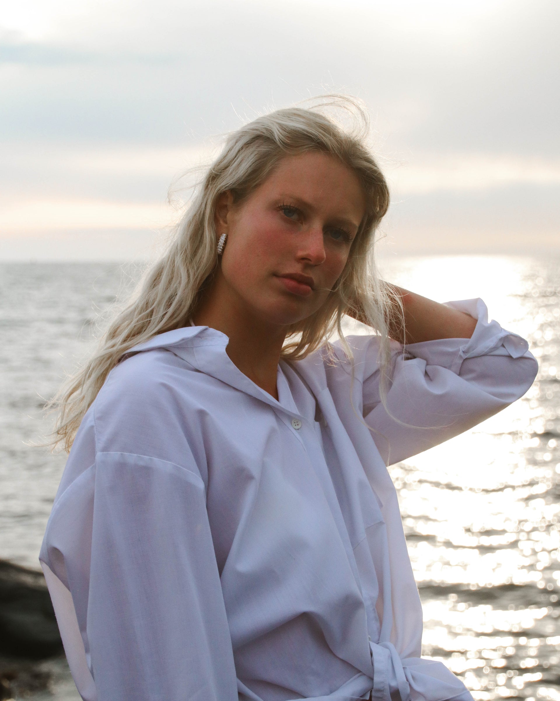 Kvinna vid havet i solnedgång med örhängen från Alora Avenue – vattentåliga smycken för en aktiv livsstil