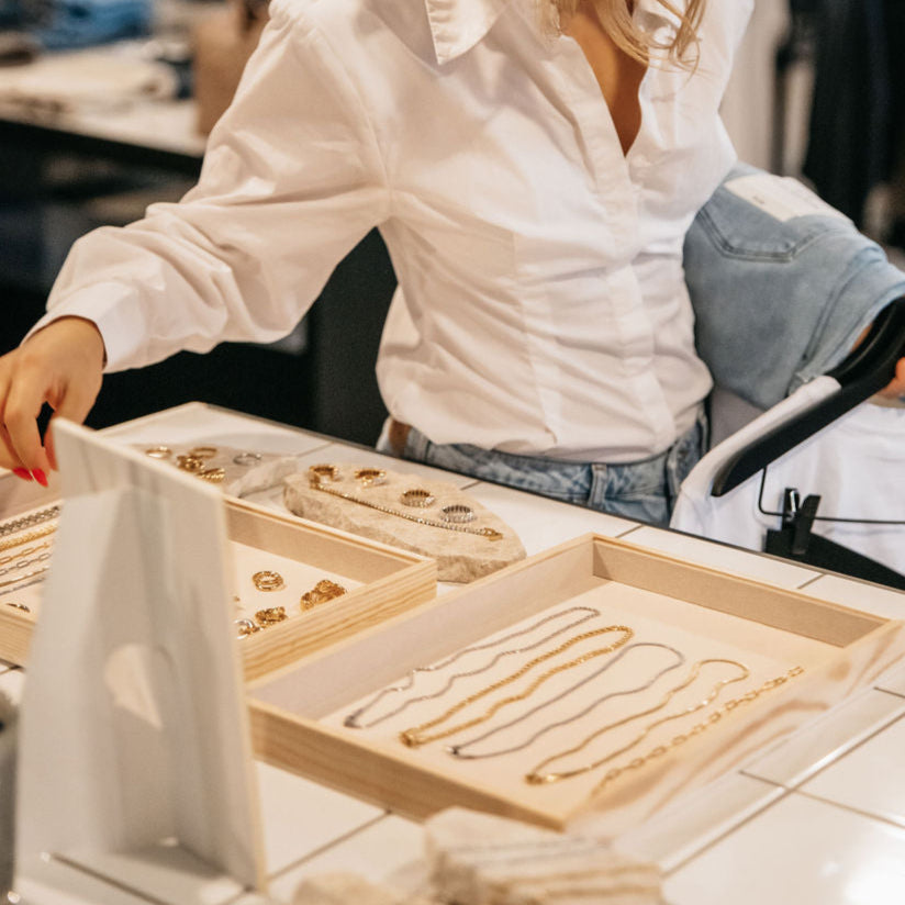 Bild från Wonder i Varberg – återförsäljare av Alora Avenue smycken. Vattentåliga halsband, armband och örhängen i 18K guldpläterat stål visas upp på butikens disk. Elegant display för exklusiva accessoarer.
