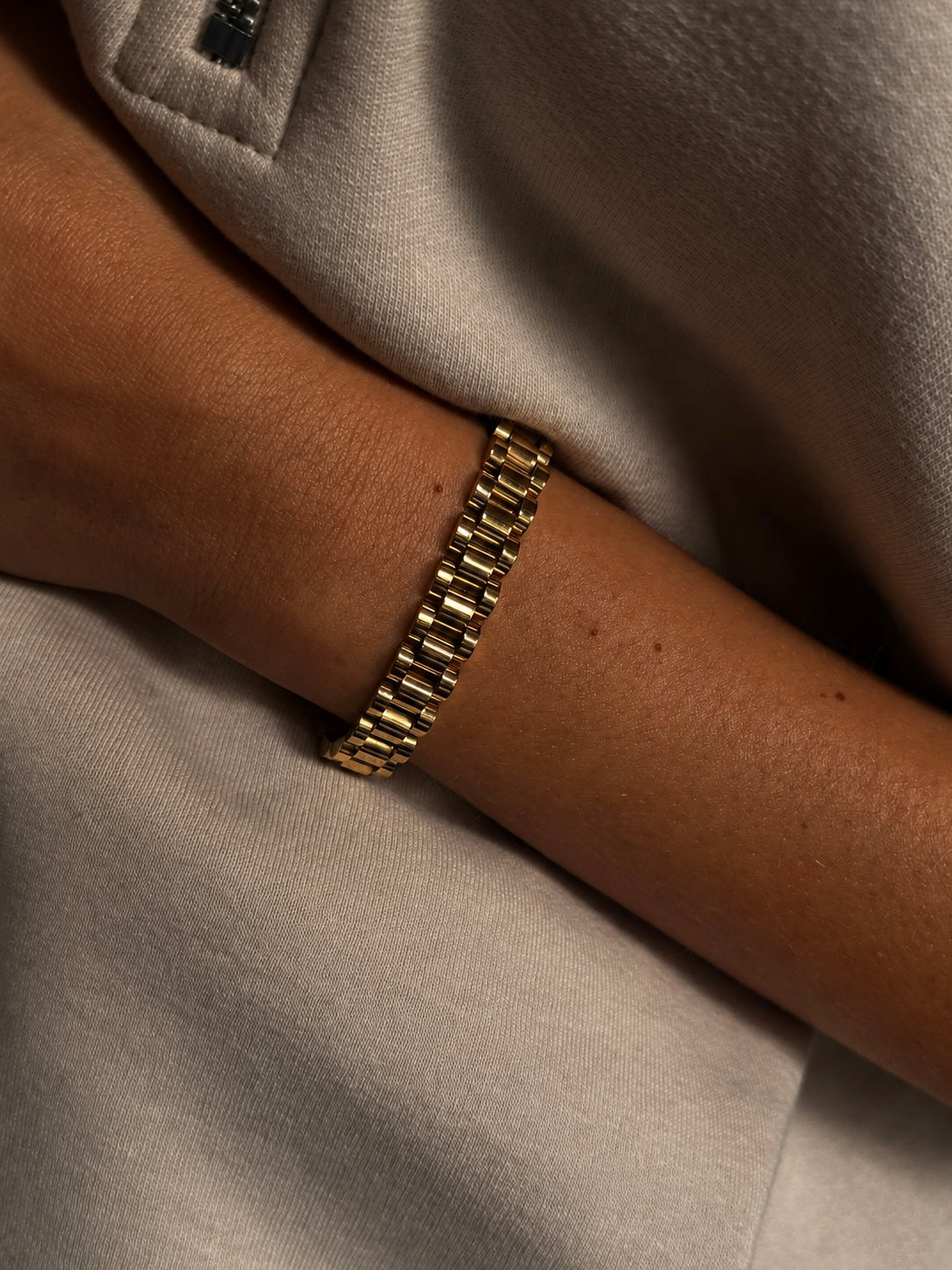 Analog Aria Wristband i guld buret på modell – brett länkarmband inspirerat av klassiska klockarmband. Vattentåligt armband i rostfritt stål med 18K guldplätering från Alora Avenue.