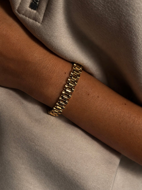 Analog Aria Wristband i guld buret på modell – brett länkarmband inspirerat av klassiska klockarmband. Vattentåligt armband i rostfritt stål med 18K guldplätering från Alora Avenue.