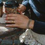 Analog Ava Wristband i guld på handled, stylat med kaffekopp och stickad tröja. Stilrent och vattentåligt armband från Alora Avenue – tidlös design för vardag och fest.