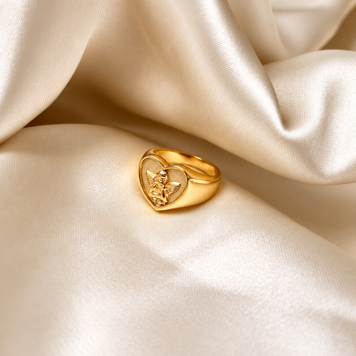 Angelic Love Ring i guld fotograferad på ljust silkestyg. Vattentåligt och allergivänligt smycke i rostfritt stål med 18K PVD-guldplätering från Alora Avenue.