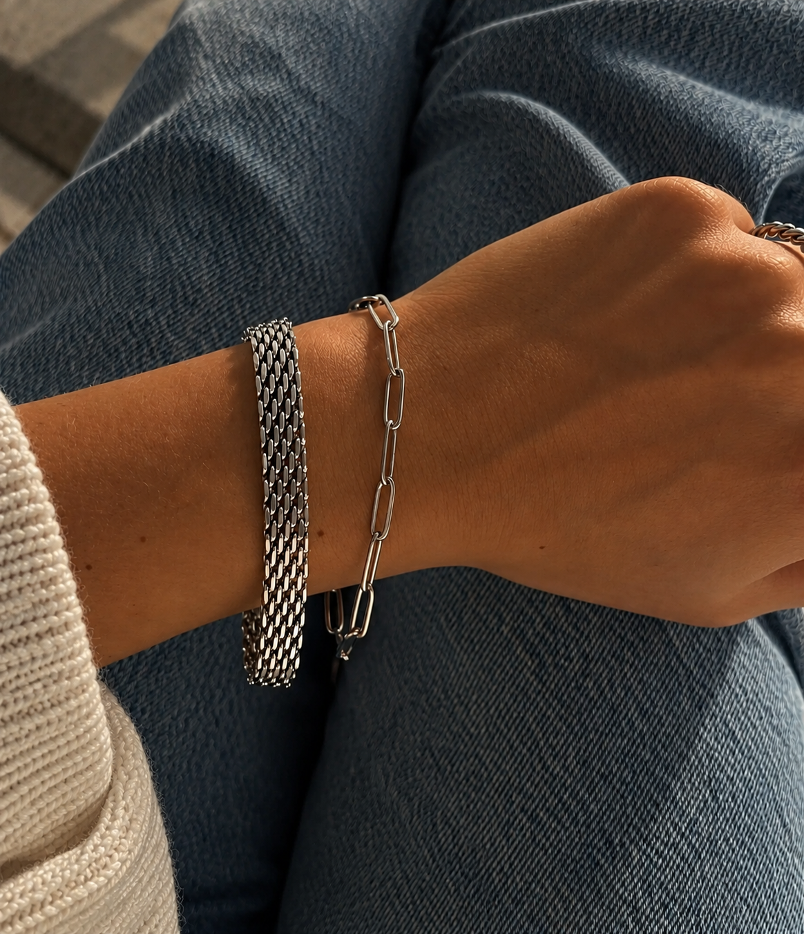 Azalea Aurora Bracelet i silver på modell mot denim, buret tillsammans med ett länkarmband. Vattentåligt och allergivänligt armband i rostfritt stål från Alora Avenue.