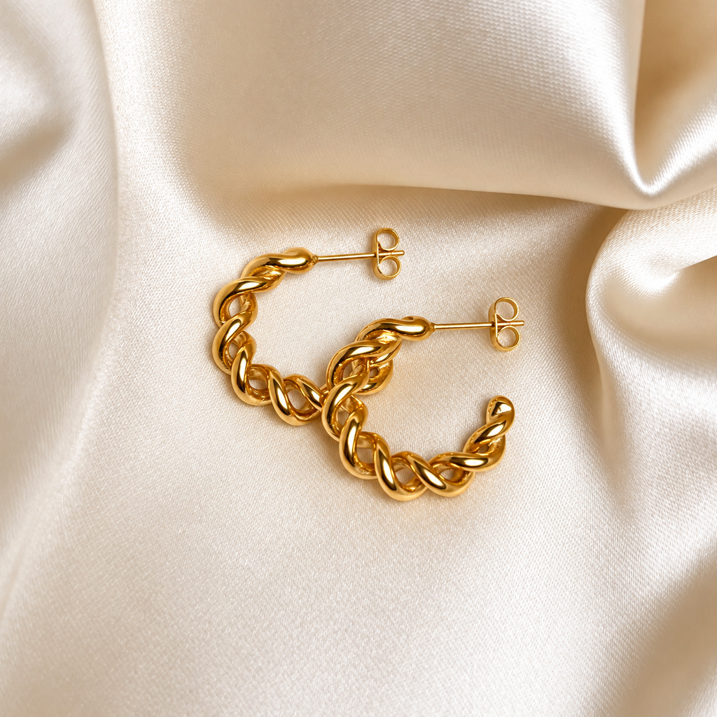 Bali Bamboo Hoops i guld fotograferade på ljust silkestyg. Vattentåliga och allergivänliga örhängen i rostfritt stål med 18K PVD-guldplätering från Alora Avenue.