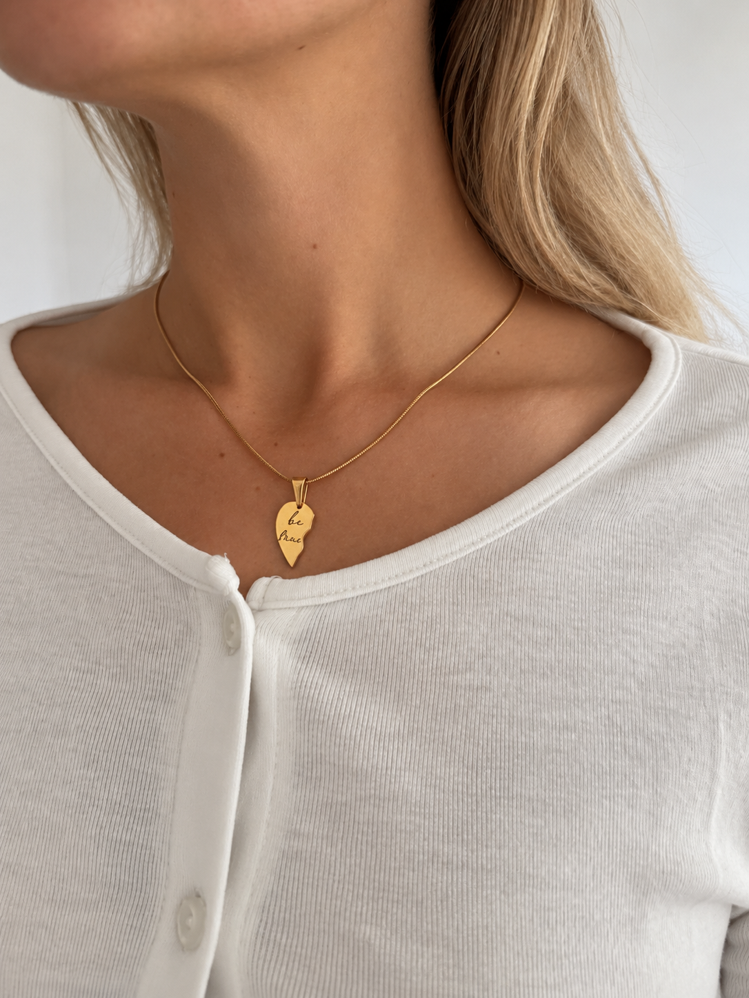 Best Friend Pendant – halva av ett tvådelat hjärta i guld graverat "best friends", buret av modell. Vänskapssmycke från Alora Avenue.