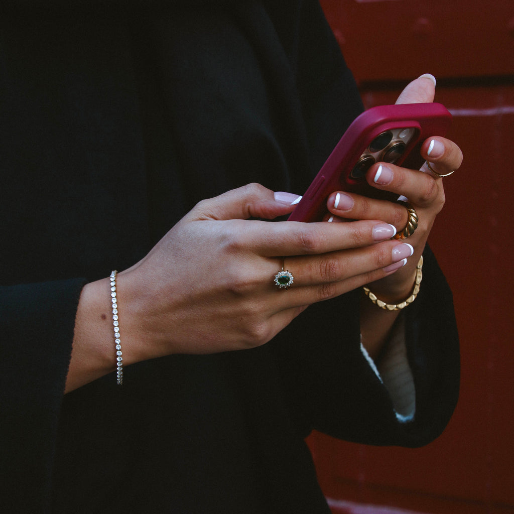 Celine Carmosé Ring i guld med grön sten, stylad på hand som håller mobil. Statementring från Alora Avenue med elegant glans och vattentålig finish.