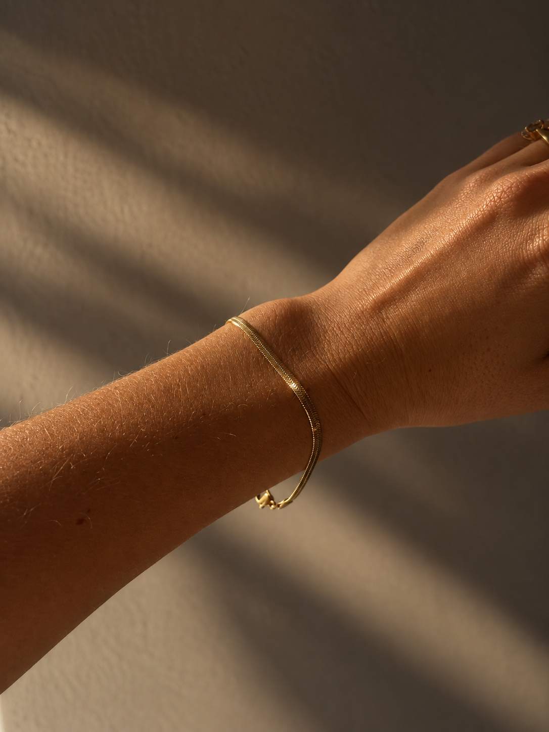 Chloe Cobra Bracelet i guld buret på modell – tunt, platt ormlänksarmband (snake chain) med blank yta. Vattentåligt armband i rostfritt stål med 18K guldplätering från Alora Avenue.