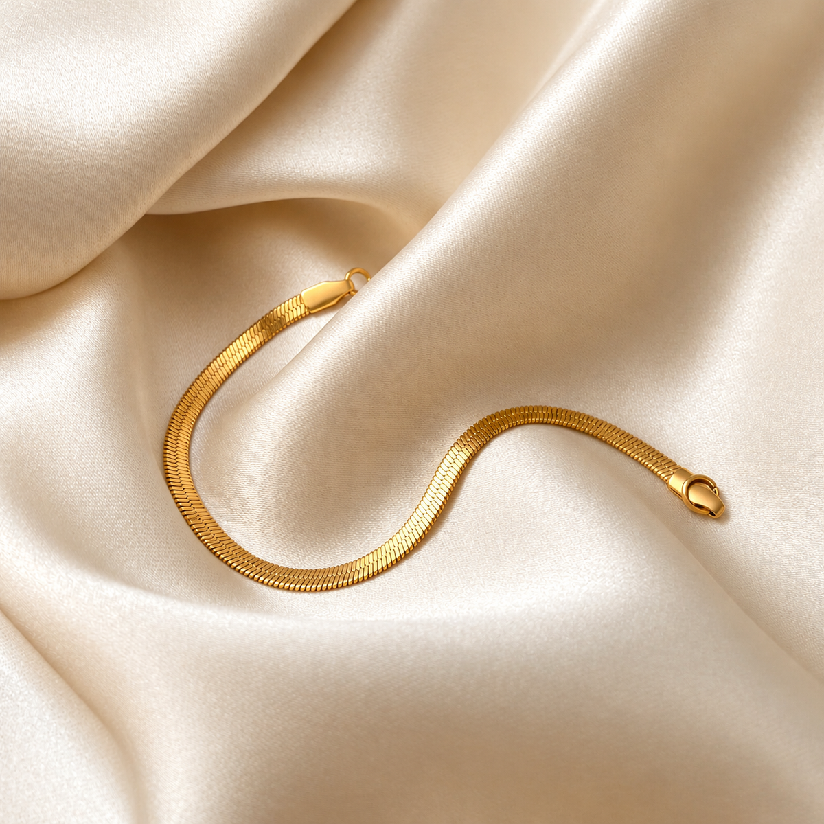 Chloe Cobra Bracelet i guld fotograferad på ljust silkestyg. Vattentåligt och allergivänligt smycke i rostfritt stål med 18K PVD-guldplätering från Alora Avenue.