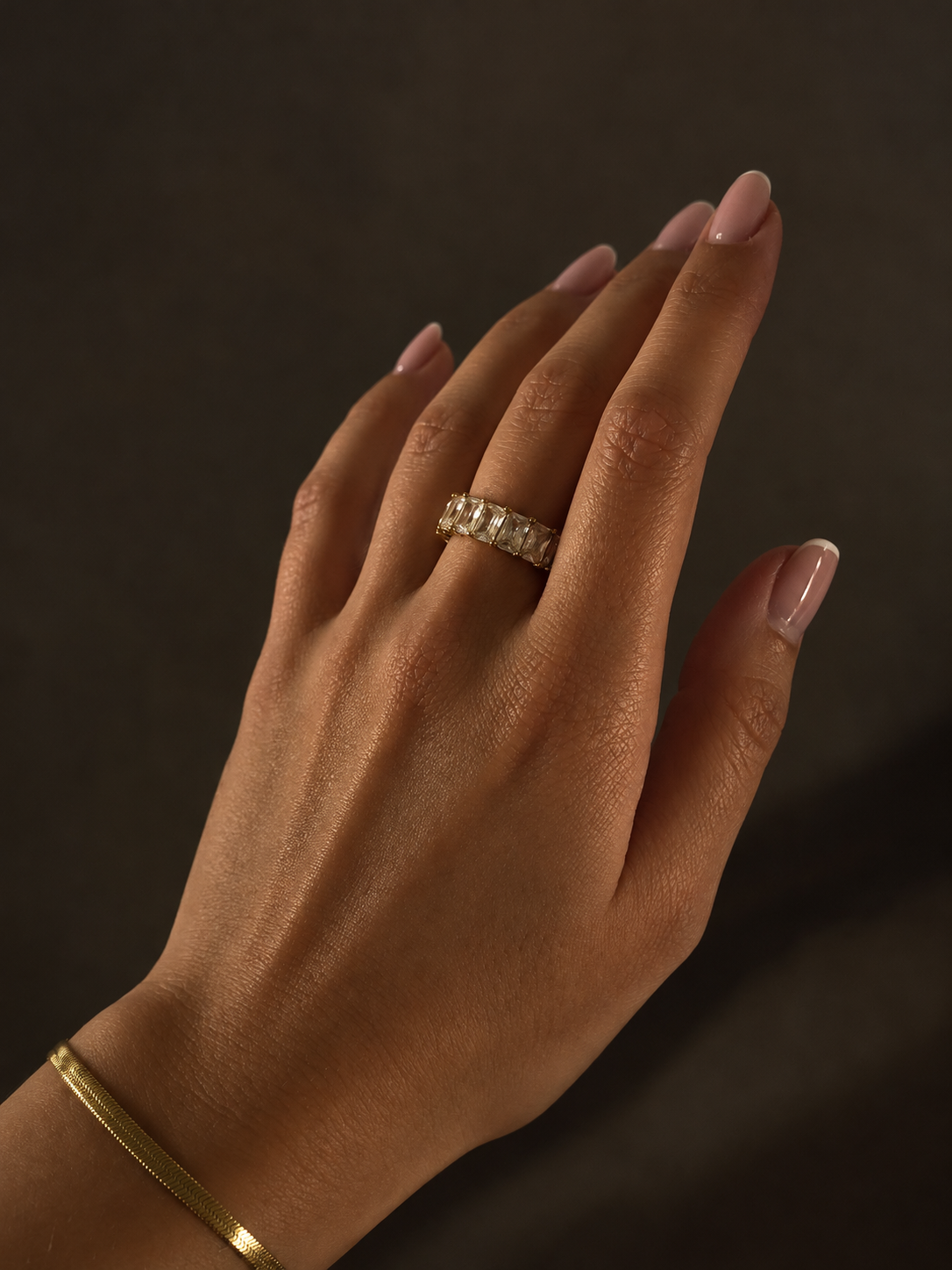 Chunky Crystal Ring i guld på modell – bred ring med rektangulära cubic zirconia-stenar, buren med Chloe Cobra Bracelet i guld. Vattentåliga smycken från Alora Avenue.