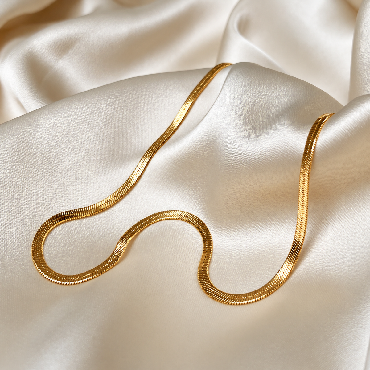 Clara Cobra Necklace i guld fotograferad på ljust silkestyg. Vattentåligt och allergivänligt smycke i rostfritt stål med 18K PVD-guldplätering från Alora Avenue.