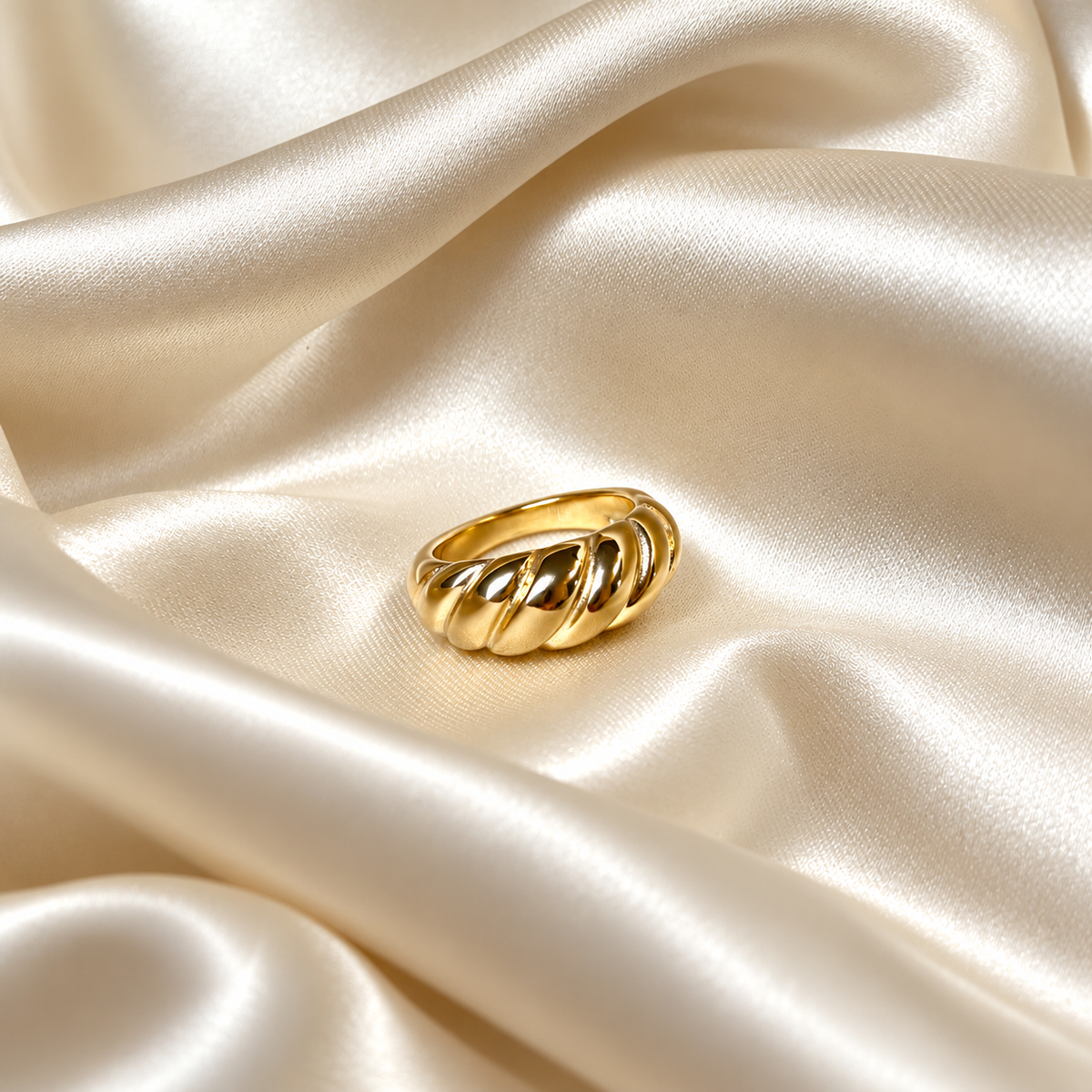 Classic Croissant Ring i guld fotograferad på ljust silkestyg. Vattentåligt och allergivänligt smycke i rostfritt stål med 18K PVD-guldplätering från Alora Avenue.