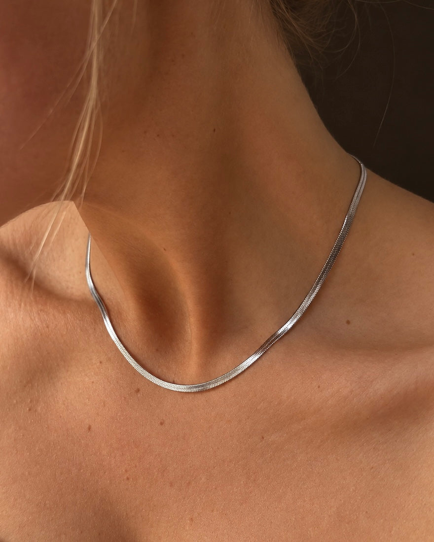 Cleo Cobra Necklace i silver på modell – platt ormlänkshalsband (snake chain) med blank yta som ligger mjukt mot nyckelbenen. Vattentåligt, allergivänligt halsband i rostfritt stål från Alora Avenue.