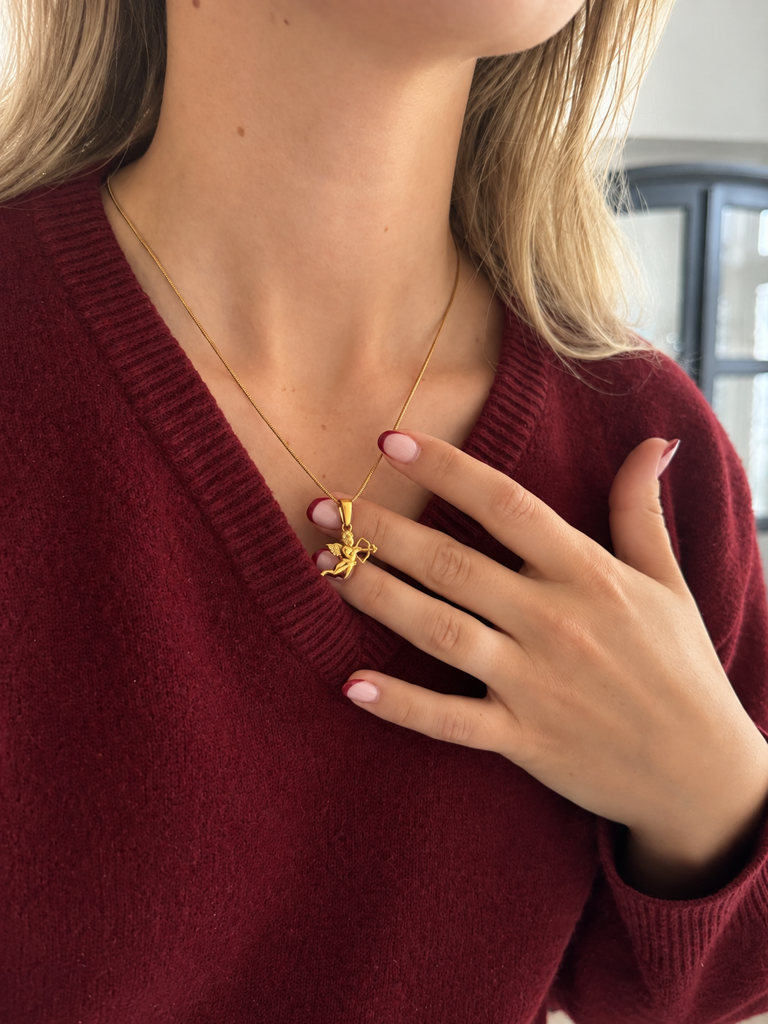 Cupid Angel Pendant – cupidhänge i guld med pilbåge, buret av modell. Vattentåligt guldsmycke från Alora Avenue.