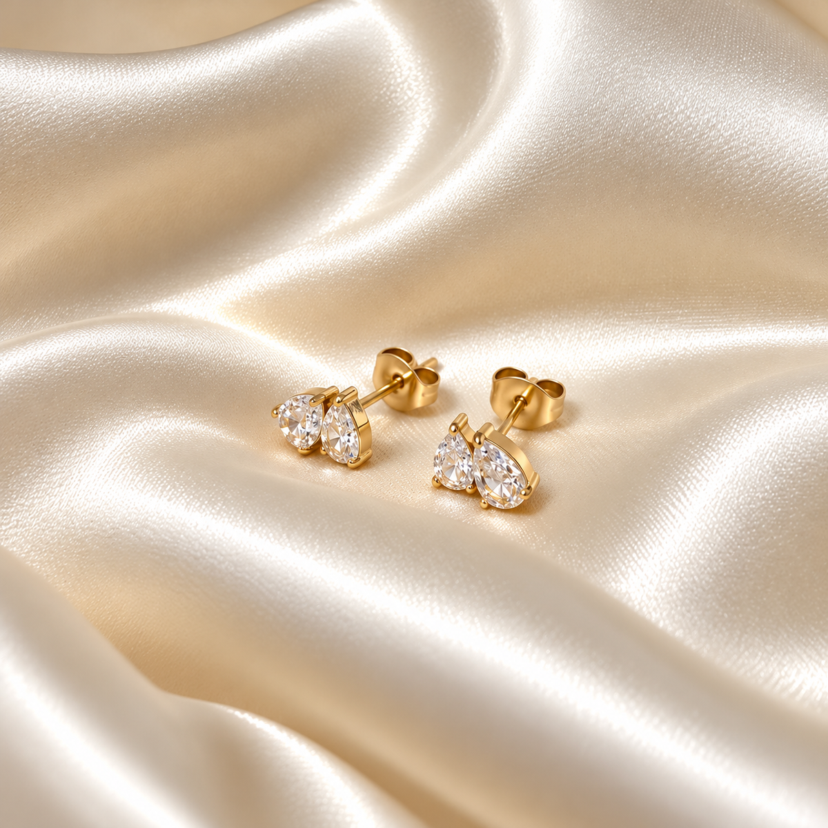 Dea Drop Earrings i guld fotograferad på ljust silkestyg. Vattentåligt och allergivänligt smycke i rostfritt stål med 18K PVD-guldplätering från Alora Avenue.