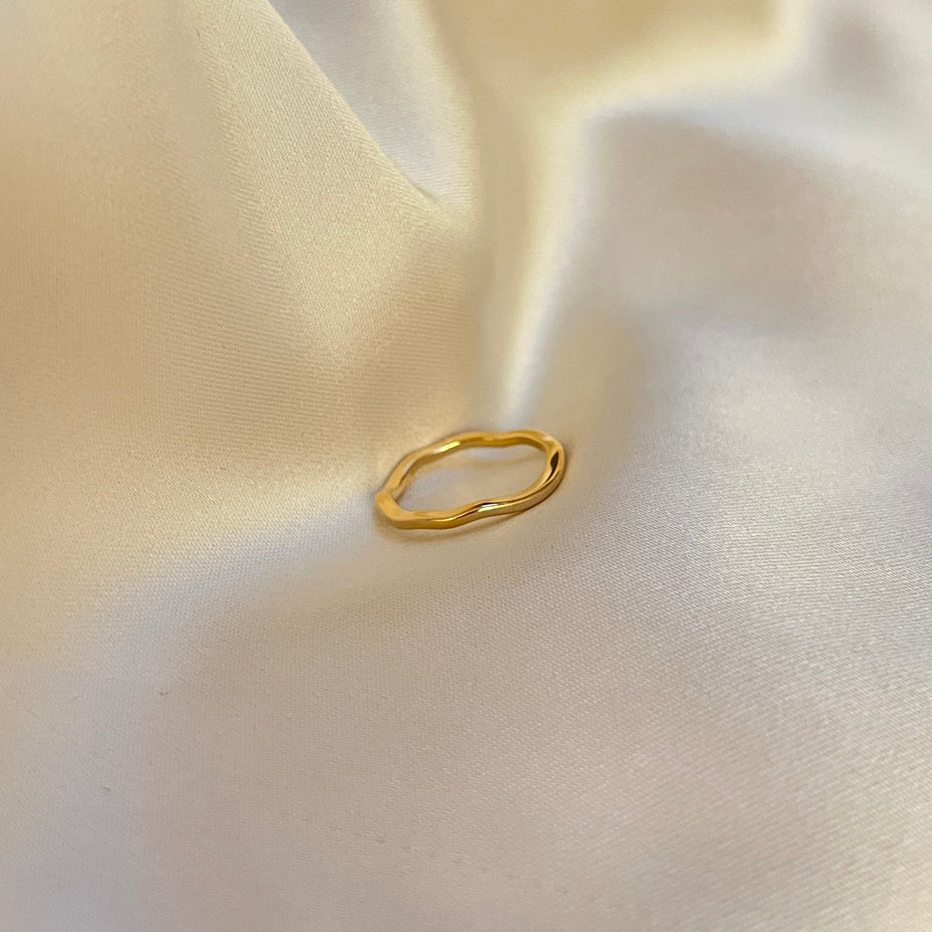 Faye Flow Ring – tunn guldfärgad ring med mjukt böljande, organisk form. Perfekt att bära ensam eller i stacking. Tillverkad i vattentåligt och allergivänligt rostfritt stål med PVD-plätering – ett stilrent smycke som håller säsong efter säsong.