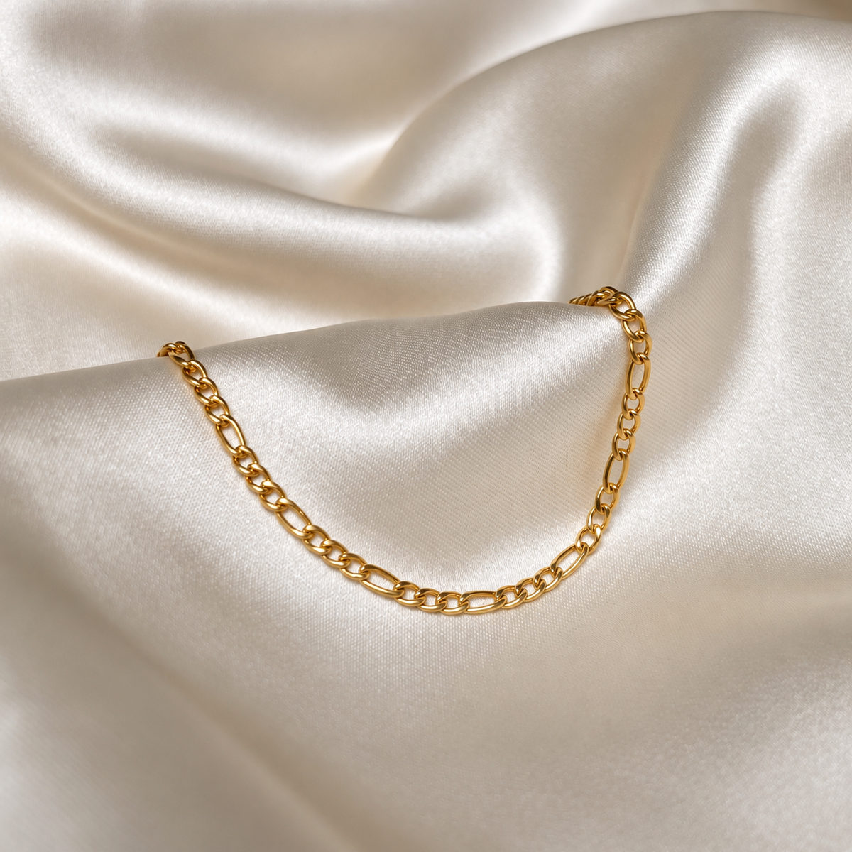 Felix Figaro Bracelet i guld fotograferat på ljust silkestyg. Vattentåligt och allergivänligt armband i rostfritt stål med 18K PVD-guldplätering från Alora Avenue.