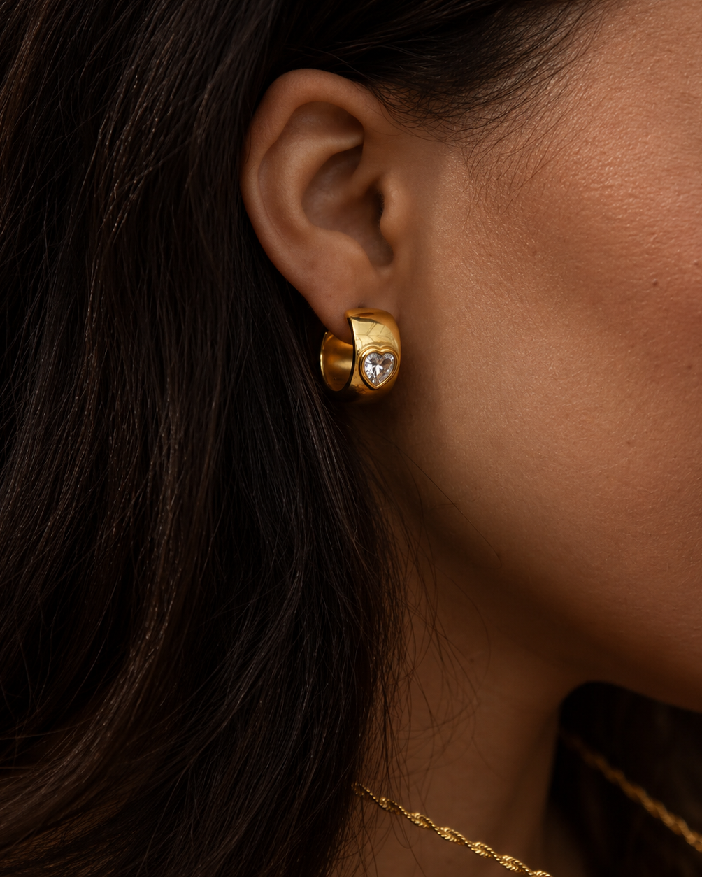 Havanna Heart Earrings i guld på modell – närbild på örat med en bred huggie med hjärtformad sten. Vattentåliga och allergivänliga örhängen i rostfritt stål med 18K PVD-guldplätering från Alora Avenue.